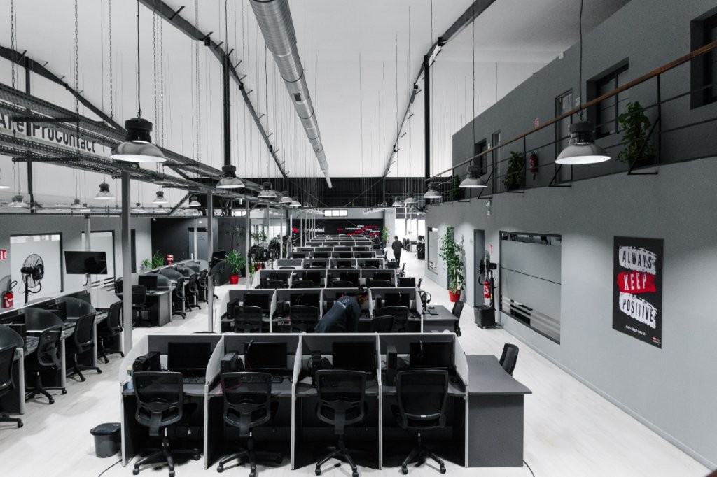 Salle de centre d'appels avec plusieurs postes de travail et éclairage suspendu.